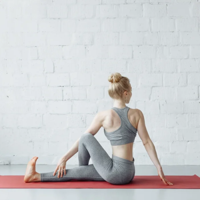 Femme en posture de torsion assise (Ardha Matsyendrasana) sur un tapis rouge, illustrant une séance de yoga du dos pour soulager les douleurs dorsales.